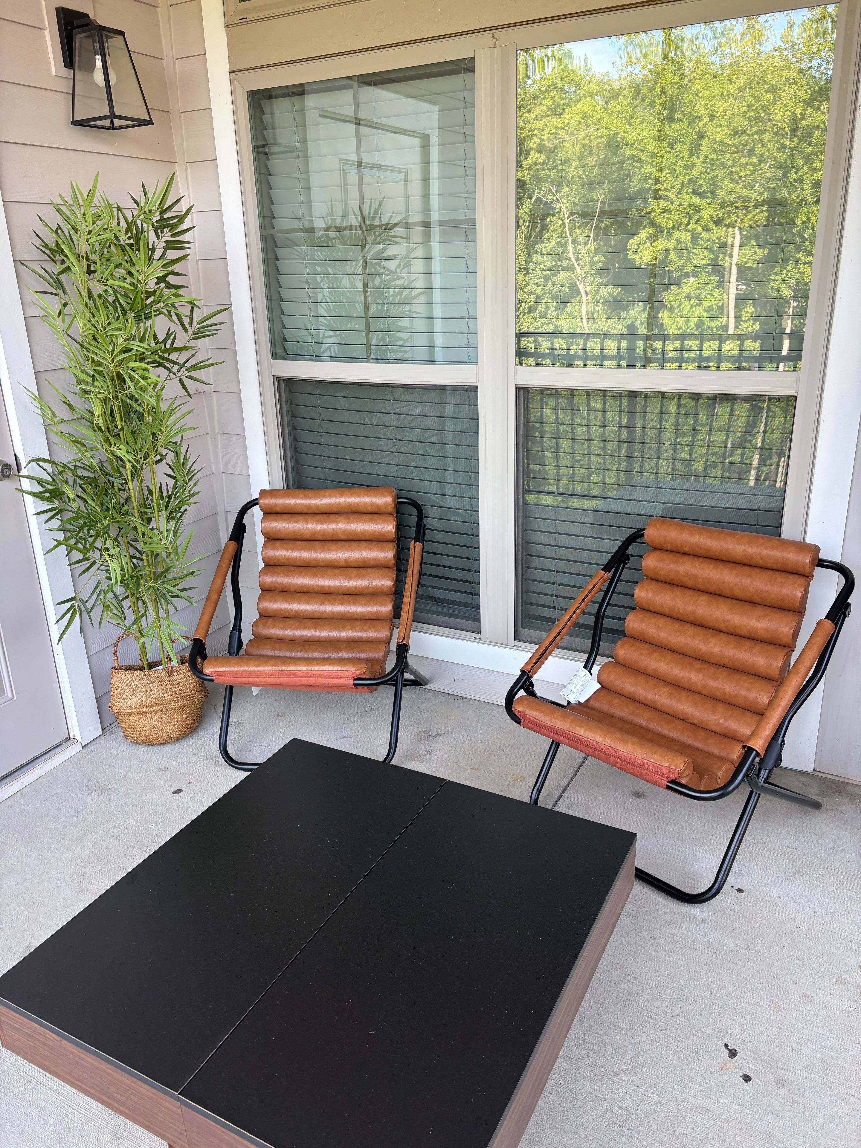 Une véranda avec deux fauteuils en cuir marron, une table noire et une plante en pot.