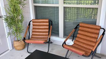 Une véranda avec deux fauteuils en cuir marron, une table noire et une plante en pot.