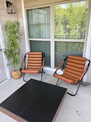 A porch with two brown leather chairs, a black table, and a potted plant.