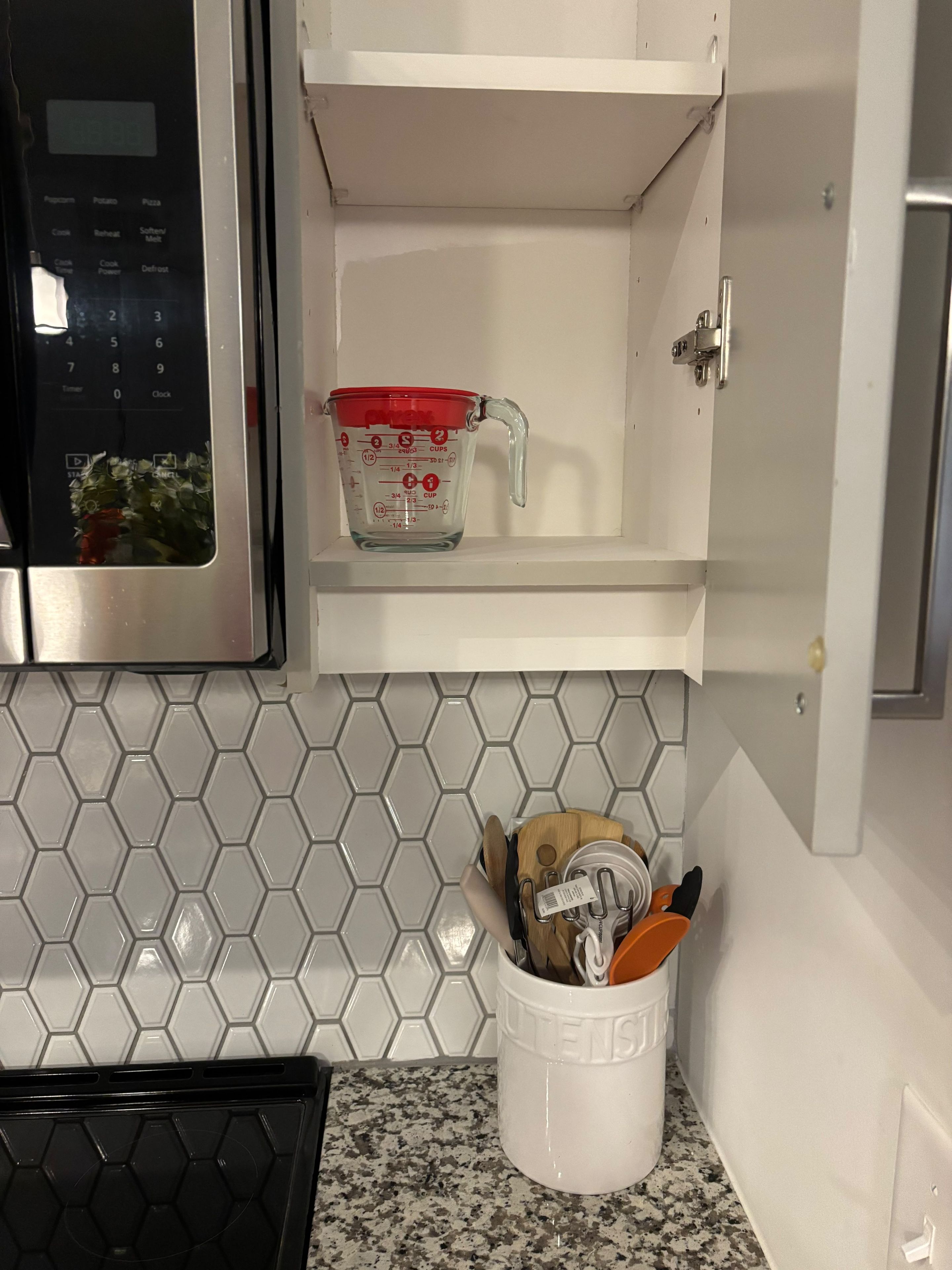 A kitchen with a microwave, a measuring cup, and a utensil holder on the countertop.