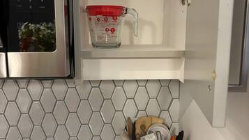A kitchen with a microwave, a measuring cup, and a utensil holder on the countertop.