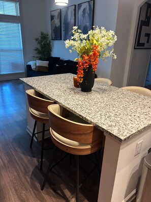 A kitchen with a granite countertop, wooden bar stools, and a vase with flowers.