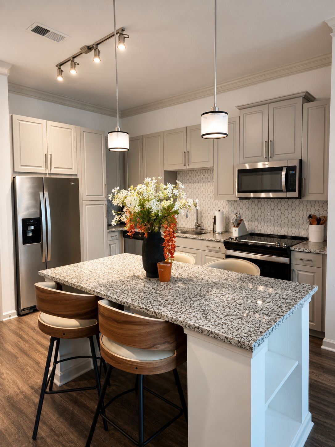 A modern kitchen with a granite island, stainless steel appliances, and pendant lighting.