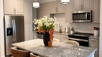 A modern kitchen with a granite island, stainless steel appliances, and pendant lighting.