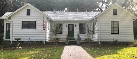 A two-story white house with a green door, a front porch, and a flag.