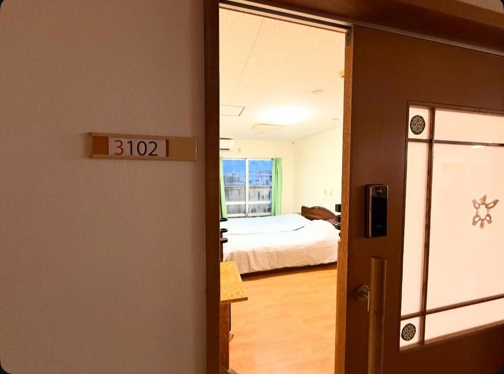 Quarto de hotel com cama, escrivaninha e janela. O número do quarto é 3102.