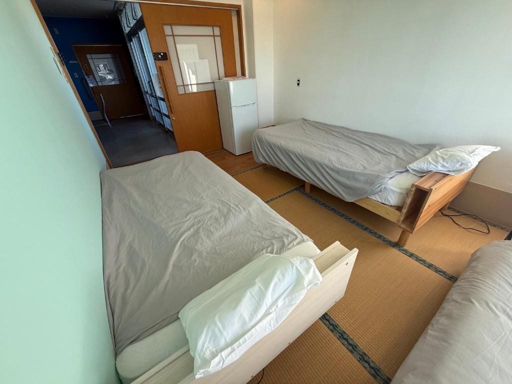A room with two single beds, a small kitchenette, and a door leading to another room.