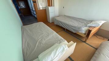 A room with two single beds, a small kitchenette, and a door leading to another room.
