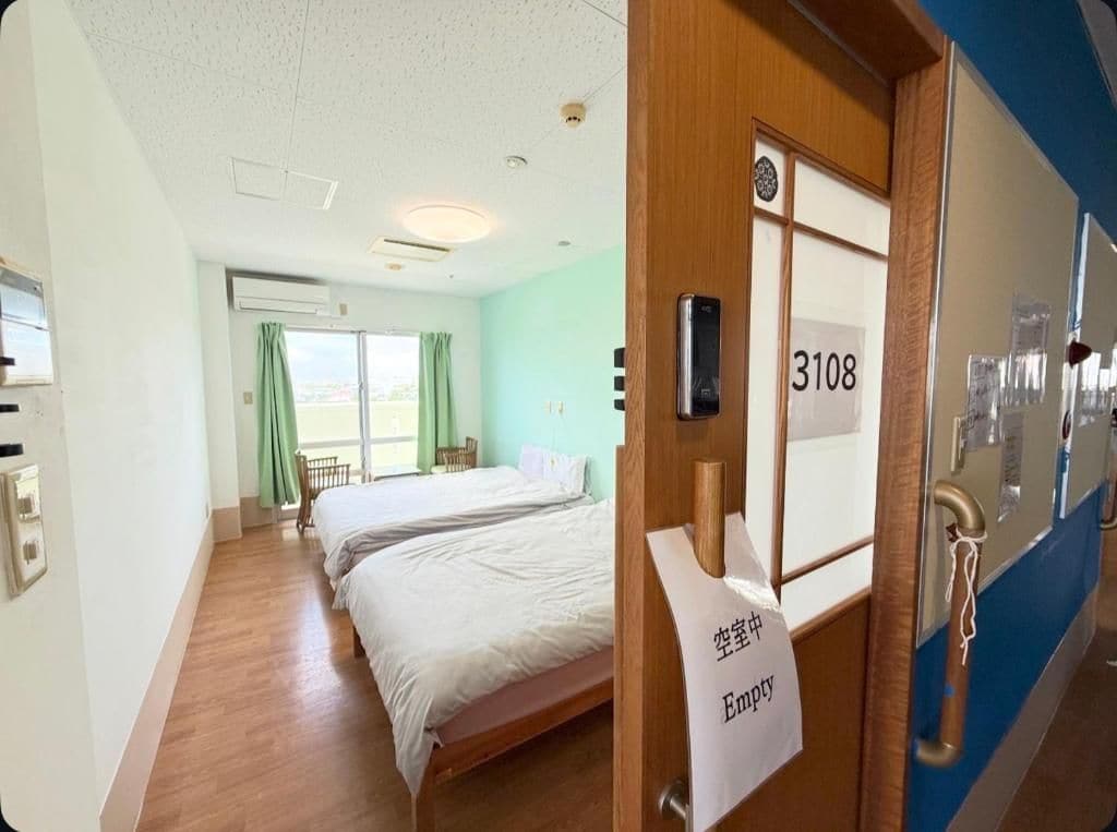 A hotel room with a bed, a window with curtains, and a door with a room number.