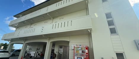 A multi-story building with a vending machine and an air conditioning unit on the ground floor.