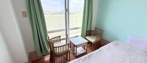 A hotel room with a bed, a small table, two chairs, and a view through a large window.
