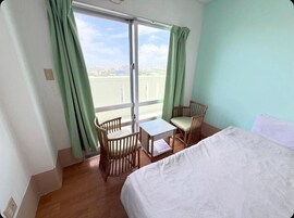 Habitación de hotel con una cama, una mesita pequeña, dos sillas y vistas amplias a través de un ventanal.