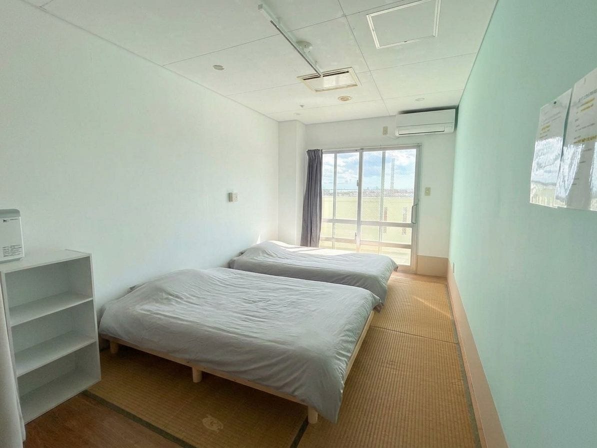 Een hotelkamer met twee bedden, een raam met gordijnen, een witte kast en een wandairconditioning.
