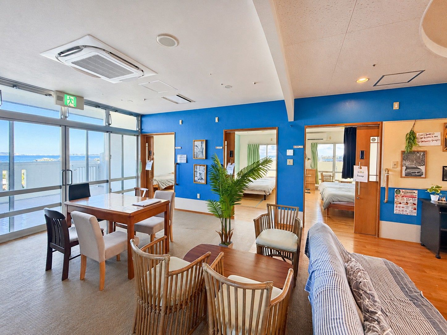 Een hotelkamer met een groot raam, een zithoek met een tafel en stoelen, en een bed met een blauw gestreepte spreideken.