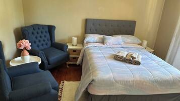 Un dormitorio con una cama, dos sillas, una mesita de noche y un florero con flores.