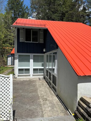 A building with a red roof, white shutters, and a concrete ground. - Charming cabin (Orford)