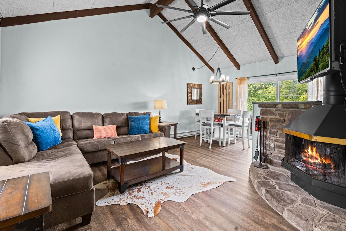 Un salon avec une cheminée en pierre, un canapé en cuir, une table basse en bois et un ventilateur de plafond.