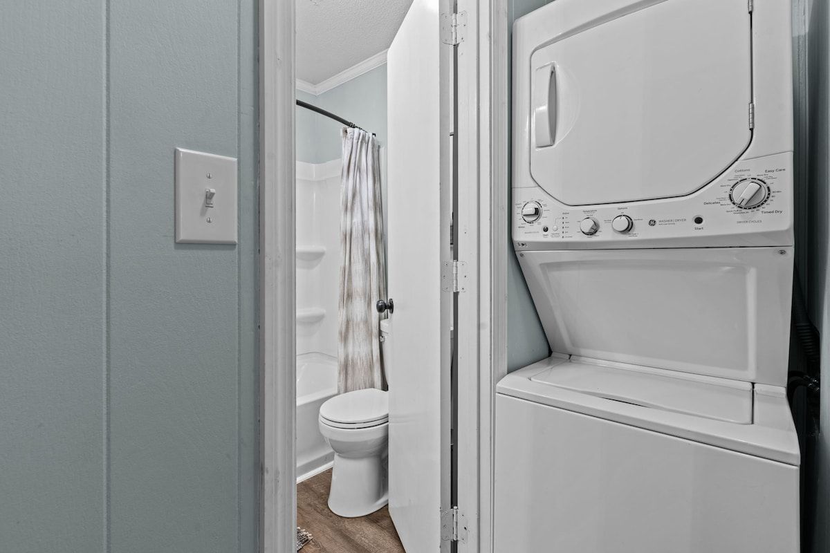 A laundry room with a washing machine and dryer, a toilet, and a shower curtain.