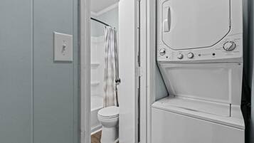 A laundry room with a washing machine and dryer, a toilet, and a shower curtain.