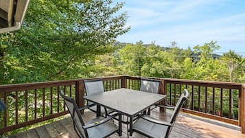 Eine Terrasse mit Tisch und Stühlen, umgeben von einem Holgitter, mit Blick auf eine bewaldete Landschaft.