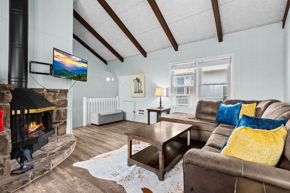 A living room with a stone fireplace, a flat-screen TV mounted on the wall, a sofa with cushions, and a wooden coffee table.