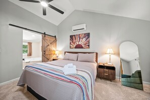 Un dormitorio con una cama, una mesita de noche, una lámpara, un aire acondicionado de pared y un espejo grande.