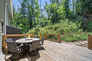 A wooden deck with a round table and wicker chairs, surrounded by greenery. - Cozy High Country Cabin Near Banner Elk (Banner Elk)