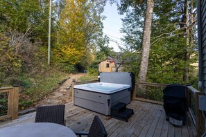 Een hottub op een houten terras, met uitzicht op een huis en bomen.