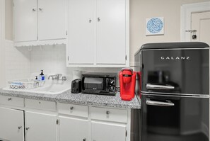 A kitchen with white cabinets, a black Galanz refrigerator, a red coffee maker, a black toaster, and a sink with a faucet. - Cloverdale Retreat 327 (Montgomery)