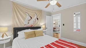 A bedroom with a bed, a ceiling fan, a nightstand, a lamp, a wall with a mirror, and a door leading to another room. - Mins to Downtown, Jackson Hosp., ASU, Maxwell AFB (Montgomery)