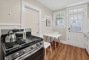 A compact kitchen with a gas stove, a kettle, and a table with chairs.