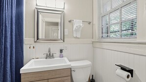 A bathroom with a white sink, a toilet, a mirror, and a window with blinds. - Mins to Downtown, Jackson Hosp., ASU, Maxwell AFB (Montgomery)