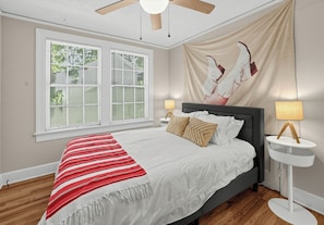 A bedroom with a bed, two bedside lamps, a window with blinds, and a ceiling fan.