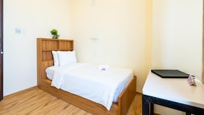 A single bed with a wooden headboard, a bedside table with a black object, and a small potted plant on the headboard. - Hotel Mo (Taguig City)