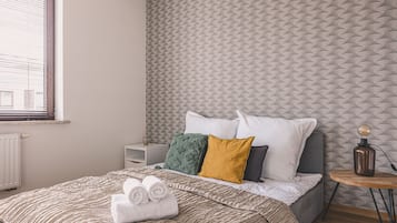 A neatly made bed with rolled towels, a bedside table with a lamp, and a patterned wall.