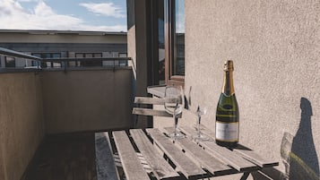 A balcony with a wooden table, two wine glasses, and a bottle of wine.