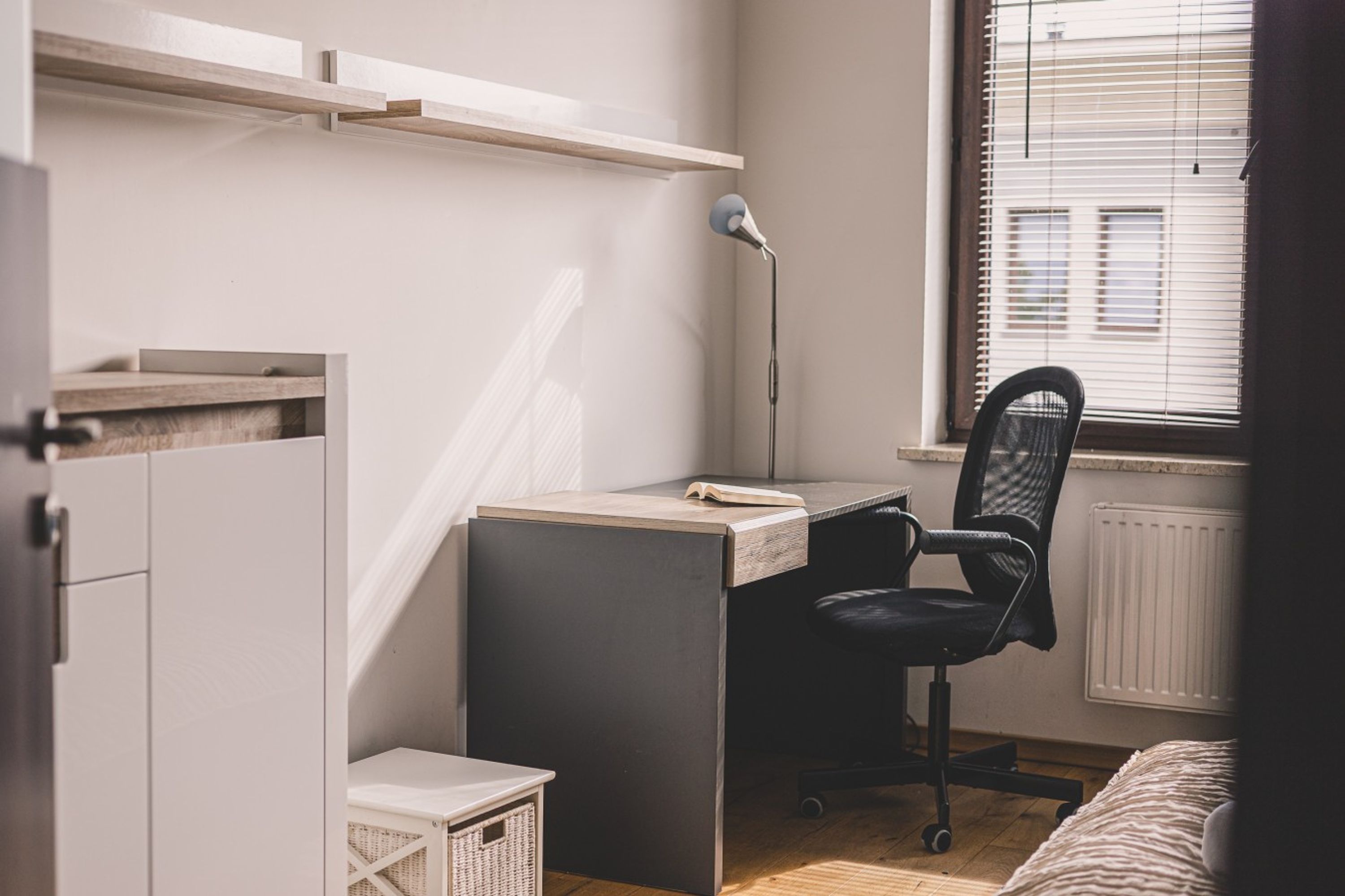 A compact bedroom with a desk, chair, and a window with blinds.