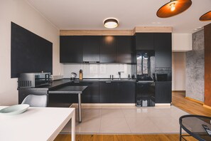 A modern kitchen with black cabinets, a stainless steel refrigerator, and a wooden dining table. - Dream 30 Du y Loft z 2 Sypialniami Bydgoszcz (Bydgoszcz)