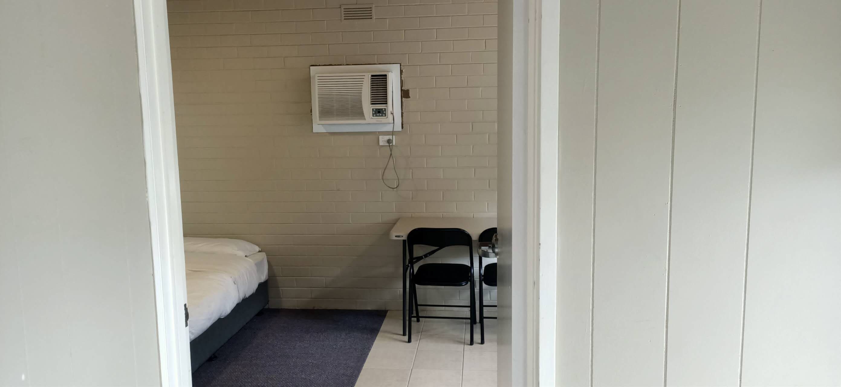 Una habitación pequeña con una cama, una silla y un aire acondicionado instalado en la pared.