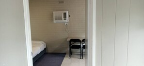 Una habitación pequeña con una cama, una silla y un aire acondicionado instalado en la pared.