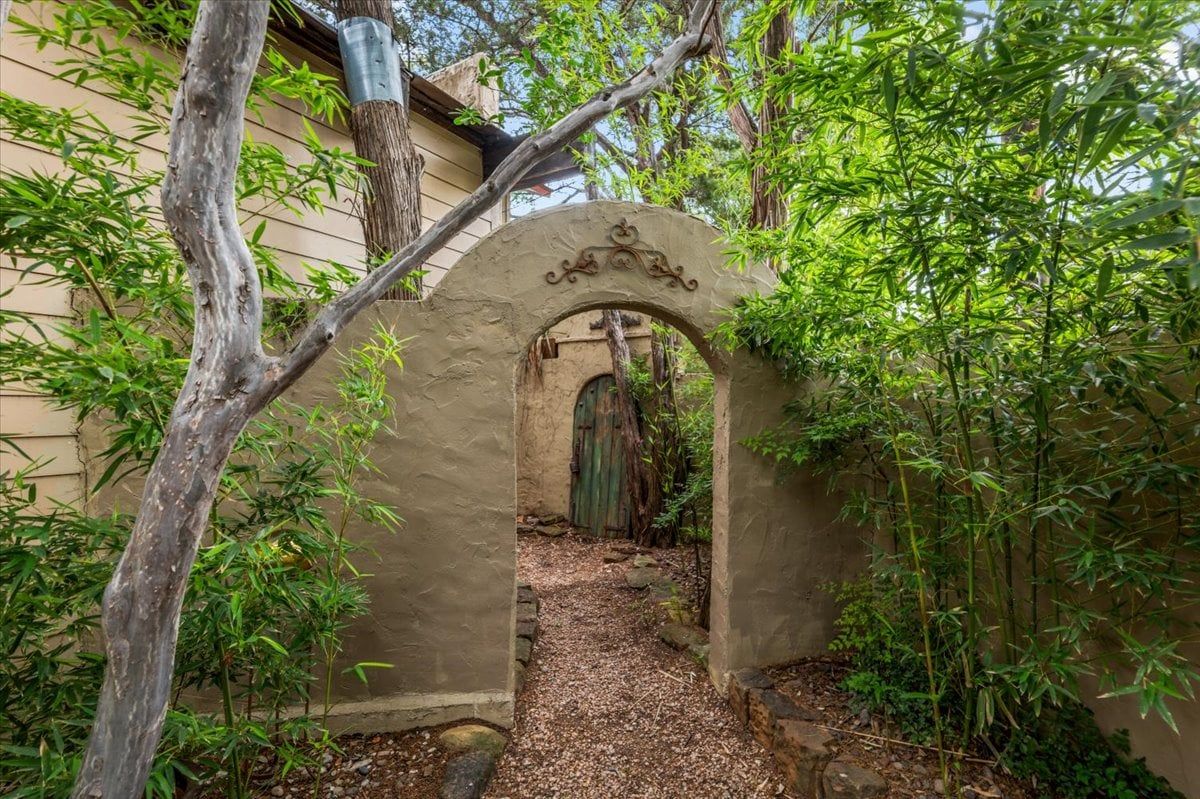 Un chemin en arc de cercle menant à l’entrée d’un bâtiment, bordé de plantes de bambou.