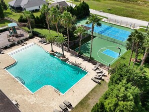 Une piscine avec un terrain de basket, des palmiers et des chaises longues.