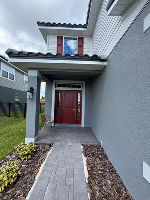 Une maison avec une porte rouge, un porche abrité et un chemin de briques menant à l’entrée.