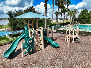 A playground with a slide and climbing structures, surrounded by a fence and palm trees. - Villa Wonderlands! in the CENTRAL FLORIDA INNOVATION DISTRIC 30 MIN FROM DISNEY! (Auburndale)