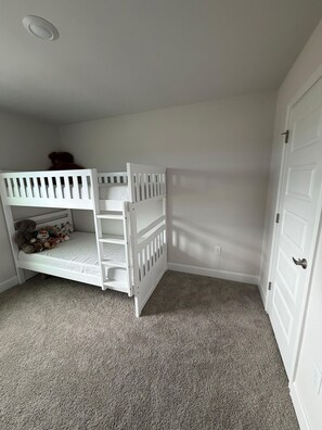 Une pièce avec un lit superposé blanc, une porte et un sol recouvert d’une moquette.