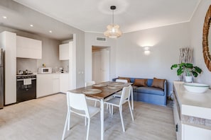 A modern kitchen with white cabinetry, a dining table with placemats, and a blue sofa with cushions.