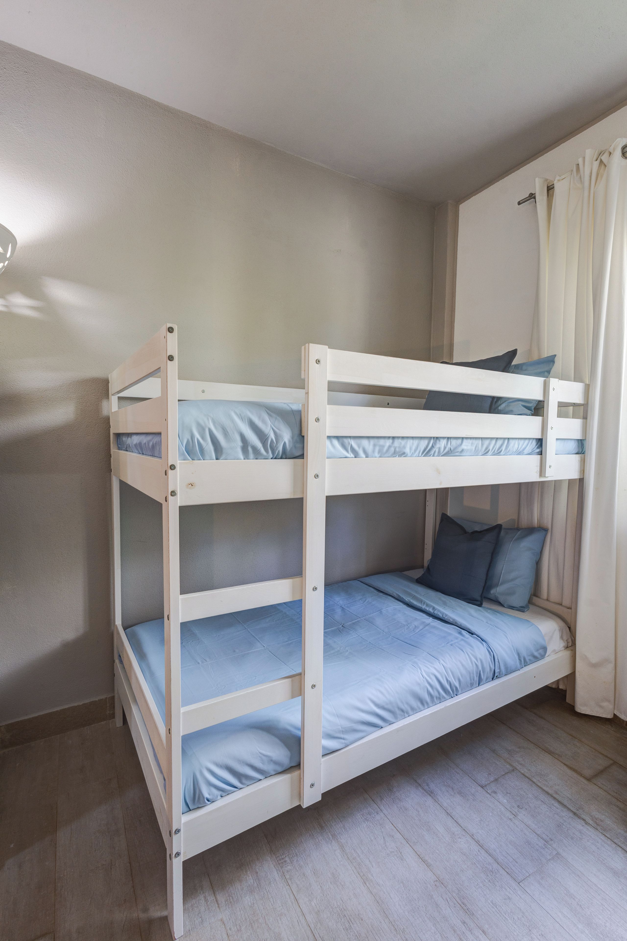 Ein Etagenbett mit drei Schlafstellen, einem Vorhang und einer Wandleuchte.
