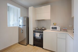 Cocina compacta con refrigerador, estufa, horno, microondas y ventana con persianas.