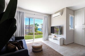 Una sala de estar moderna con un televisor grande, un sofá y vistas a un jardín y una piscina.