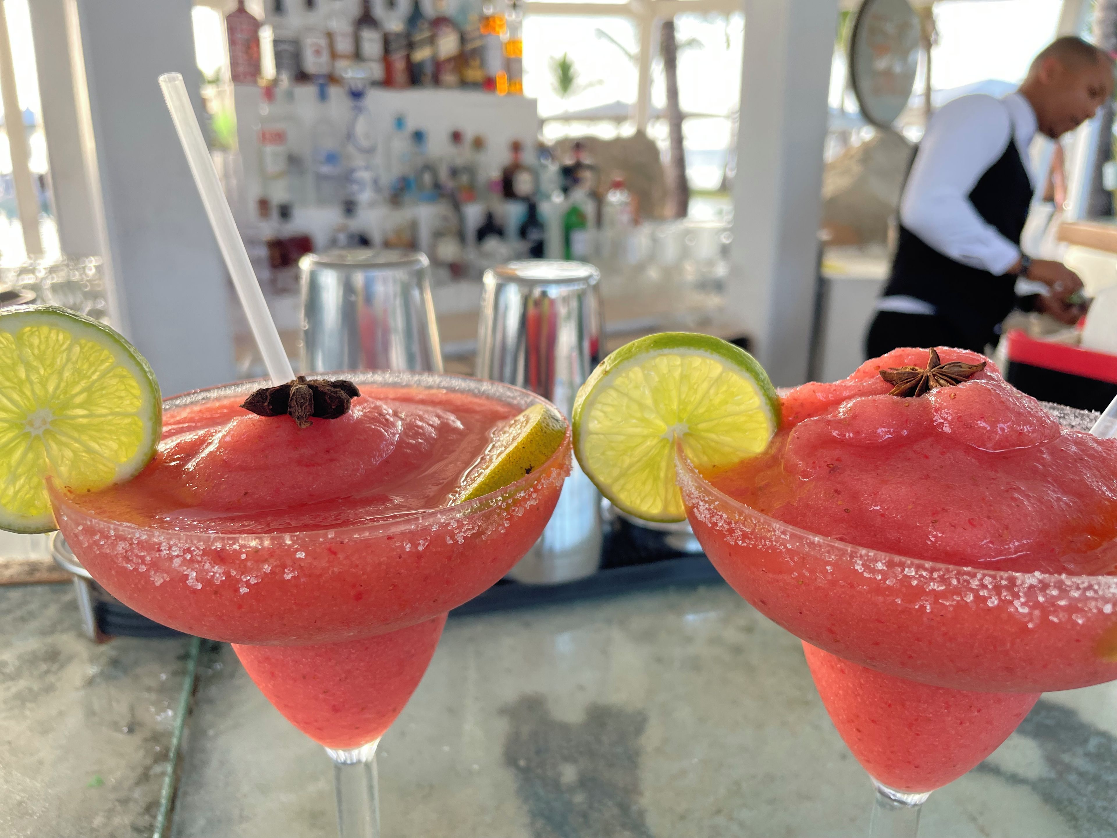 Two drinks with lime slices and star anise garnishes on a bar counter.